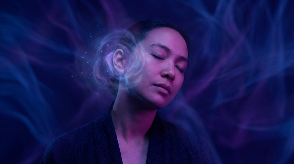Femme méditant avec des lueurs d'énergie et des étincelles autour de l'oreille gauche, sur un fond bleu-violet mystique.